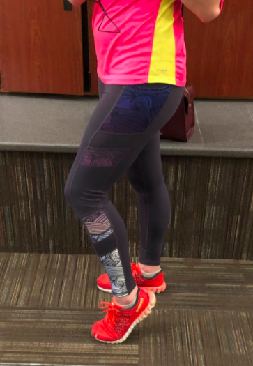 The reviewer is wearing high-rise leggings with a black, pink, and violet pattern, paired with vibrant red sneakers.