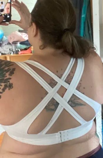 A reviewer modeling the back of a white sports bra with four crisscrossed straps