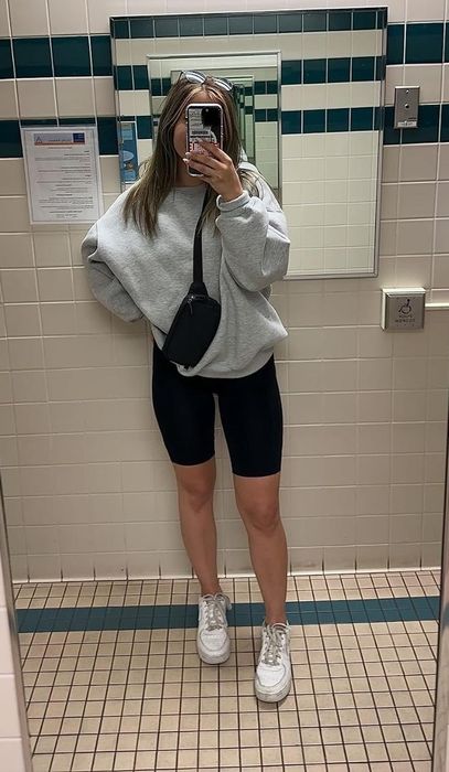 Person snapping a mirror selfie dressed in an oversized sweatshirt, shorts, sneakers, and a crossbody bag