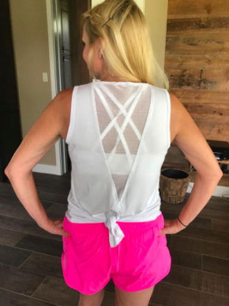Reviewer models a white tie-back tank paired with pink running shorts