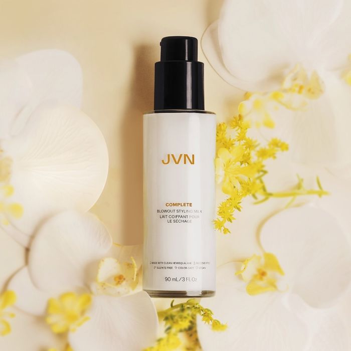 A bottle of JVN hair serum, elegantly displayed among white and yellow flowers, as featured in a shopping article.