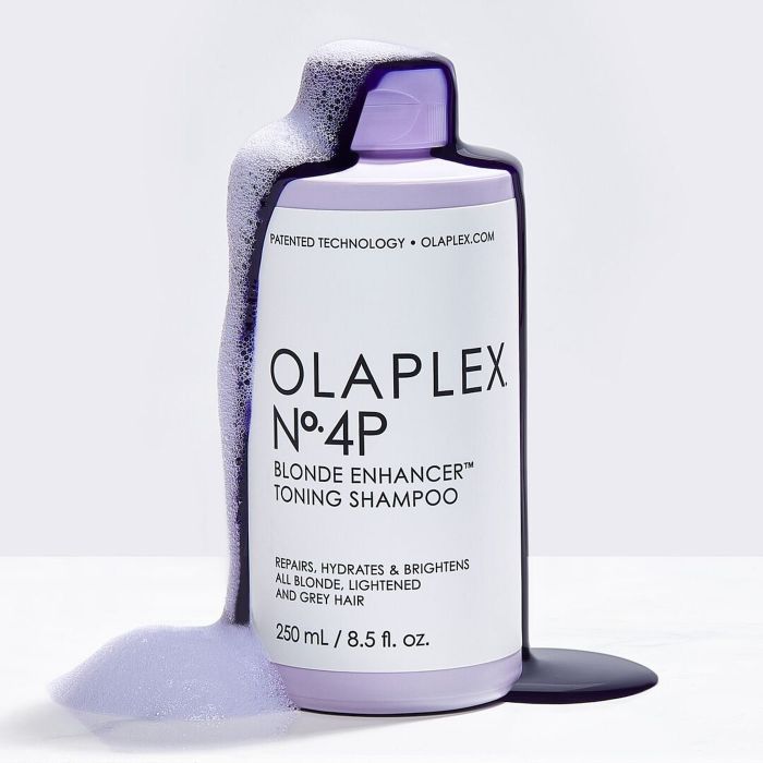 A bottle of Olaplex No.4P Blonde Enhancer Toning Shampoo with overflowing shampoo, specifically formulated for blonde, lightened, and grey hair