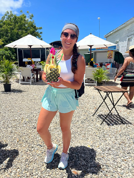A reviewer enjoying a pineapple beverage at a vibrant outdoor tropical market, dressed in relaxed summer clothing
