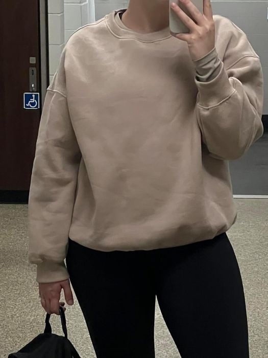 Individual in a simple sweatshirt and leggings capturing a mirror selfie, partially showing their face