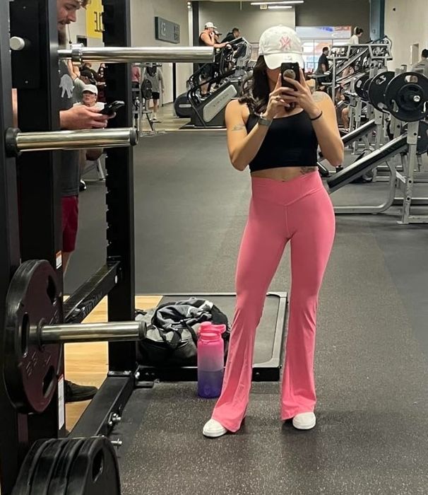 Individual in pink workout gear capturing a mirror selfie at the gym