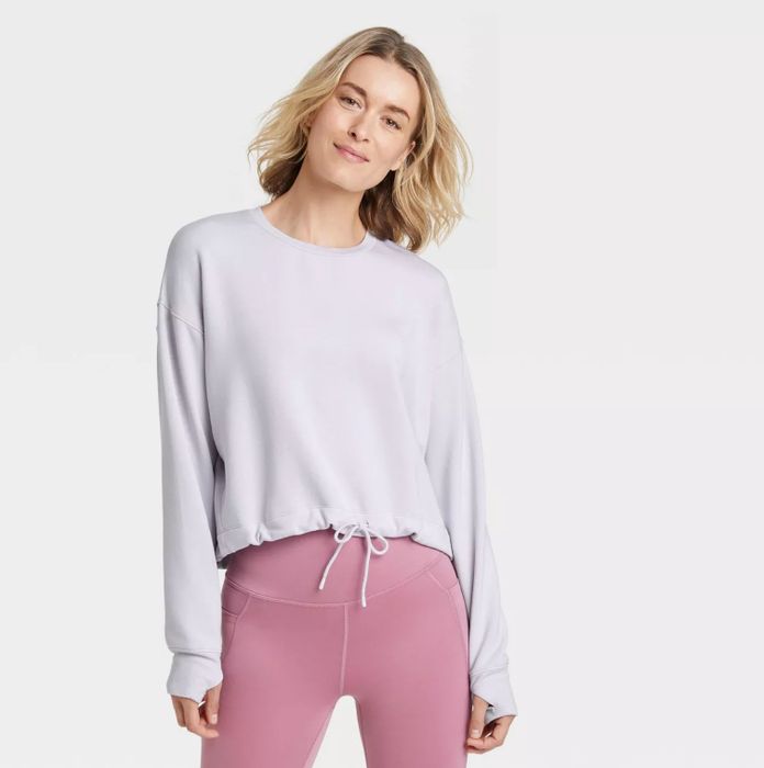 The model is styled in a white pullover with a tied waist, paired with pink leggings.