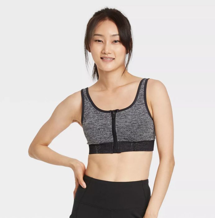 A model wearing the light gray zip-up bra with black accents, paired with black bottoms