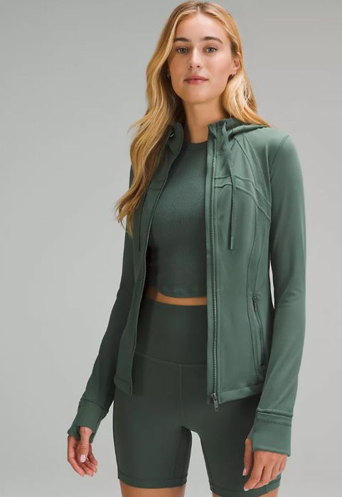 model wearing a dark green zip-up jacket with a matching top and shorts set
