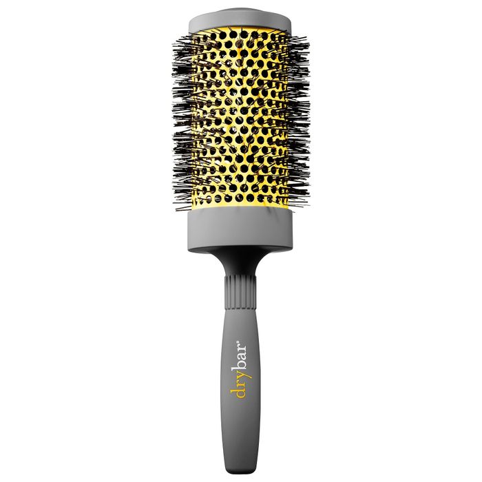 A round brush with a black handle and a gold barrel, featuring black bristles and the "drybar" logo prominently displayed on the handle.