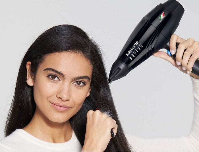 A woman demonstrates a compact hair dryer, emphasizing its lightweight construction. The text notes it weighs under 1lb, making it 40% lighter than competing models.