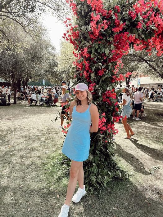 Reviewer in a casual sleeveless dress and sneakers standing in front of a flower arch in a park
