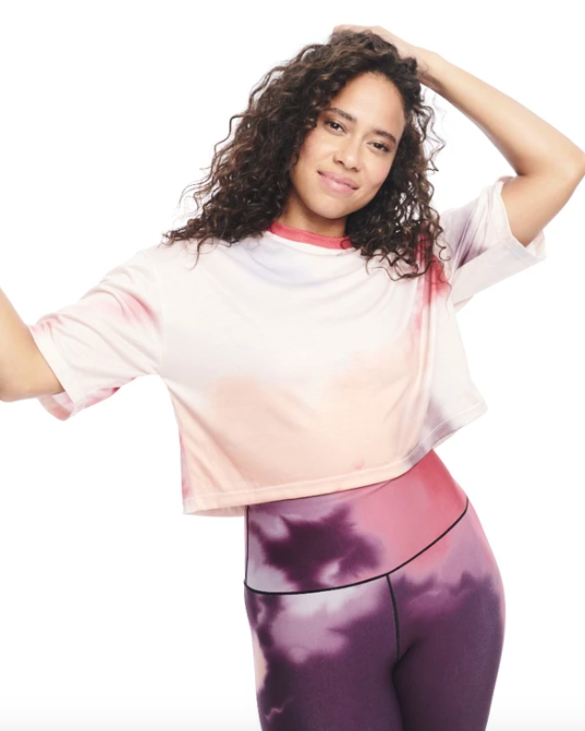 The model is dressed in a Day/Won tie-dye crop top featuring pink, red, and purple hues, paired with matching purple tie-dye leggings.