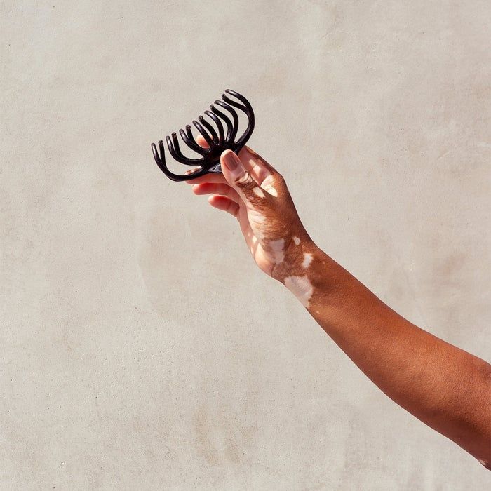 A hand holding a sleek black hair claw clip against a neutral-toned background