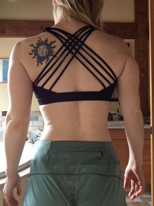 Person in a sports bra featuring a crisscross back design and casual trousers, showcasing a tattoo on their upper back