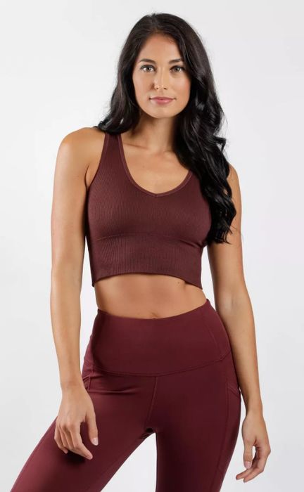 The model is styled in a burgundy crop top paired with coordinating leggings.