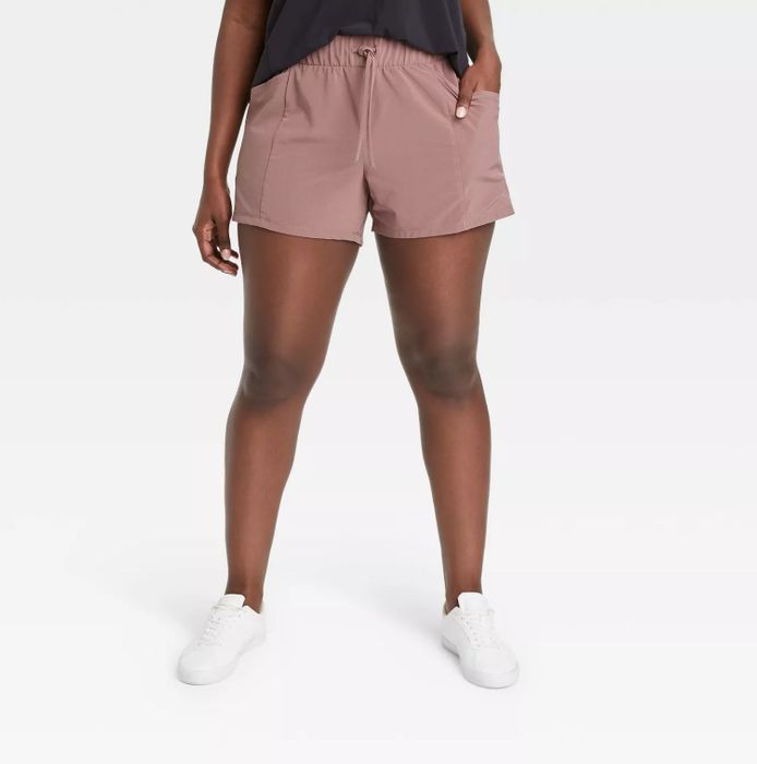 A model styled in pink shorts paired with a black top and white shoes, casually posing with one hand in the pocket
