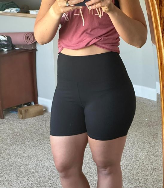 Individual trying on black shorts in front of a mirror, likely for a shopping review