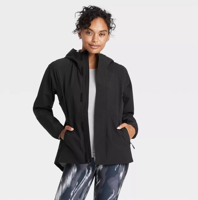 A model wearing the black jacket paired with blue tie-dye leggings and a gray top
