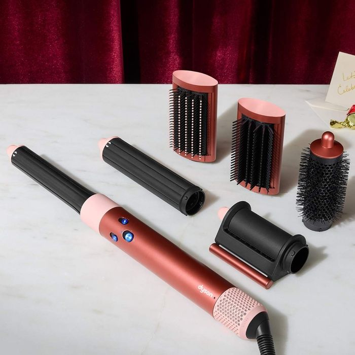 A collection of hair styling tools, including a curling wand and multiple detachable brush attachments, neatly arranged on a table.