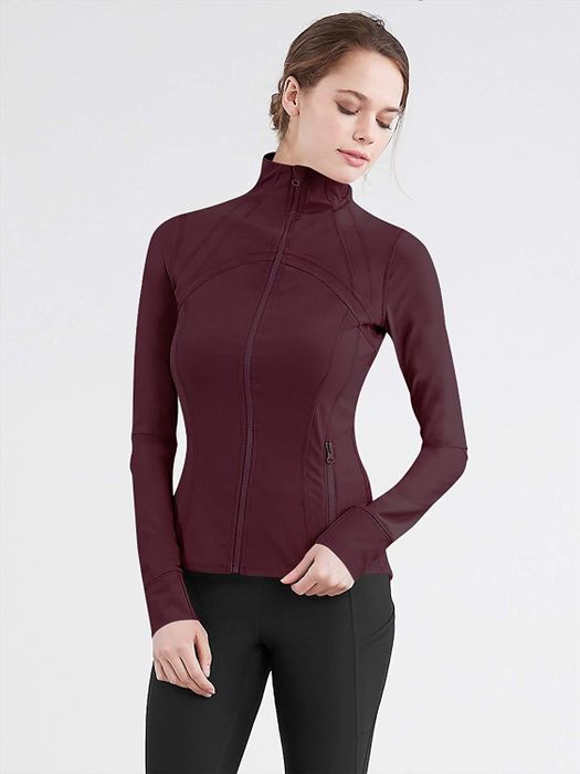 The model is dressed in a long-sleeve, wine-colored zip-up track jacket paired with sleek black leggings.