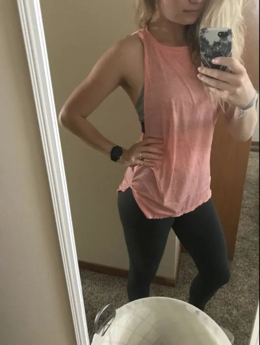 A reviewer wearing a pink tank that reaches mid-hip and features a classic crewneck design