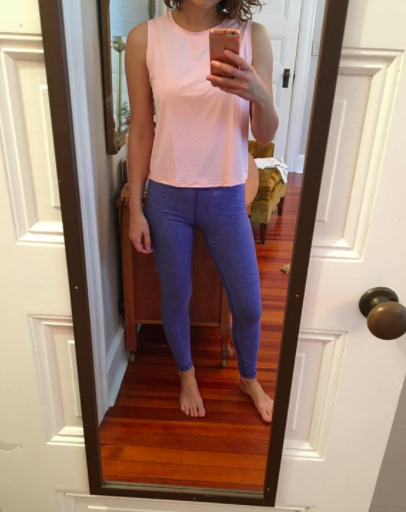 The reviewer is wearing a vibrant pink muscle tank with dark blue leggings, capturing a selfie mid-workout.
