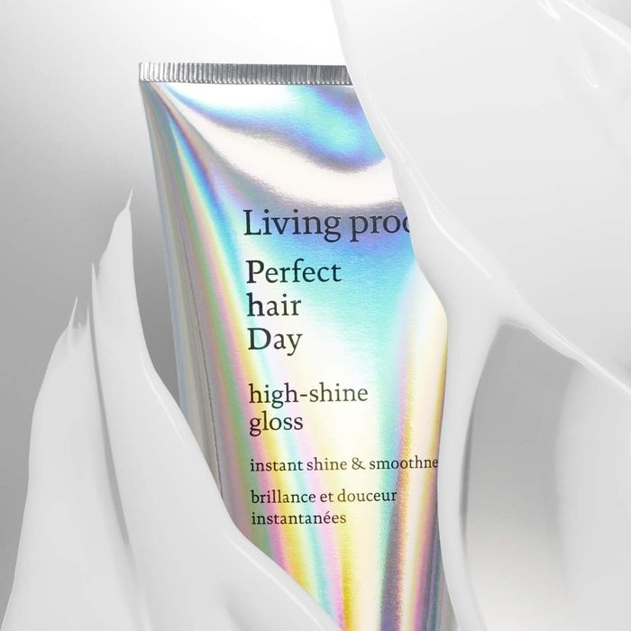 A tube of Living Proof high-shine gloss, with text emphasizing its instant shine and smoothing benefits, set against a textured background.