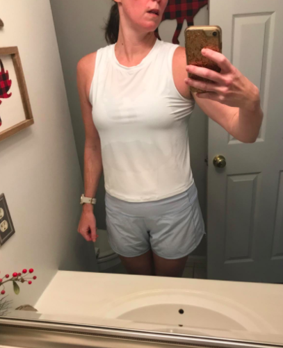 The reviewer is seen in the same style tank, this time paired with light gray shorts, posing in front of a bathroom mirror.
