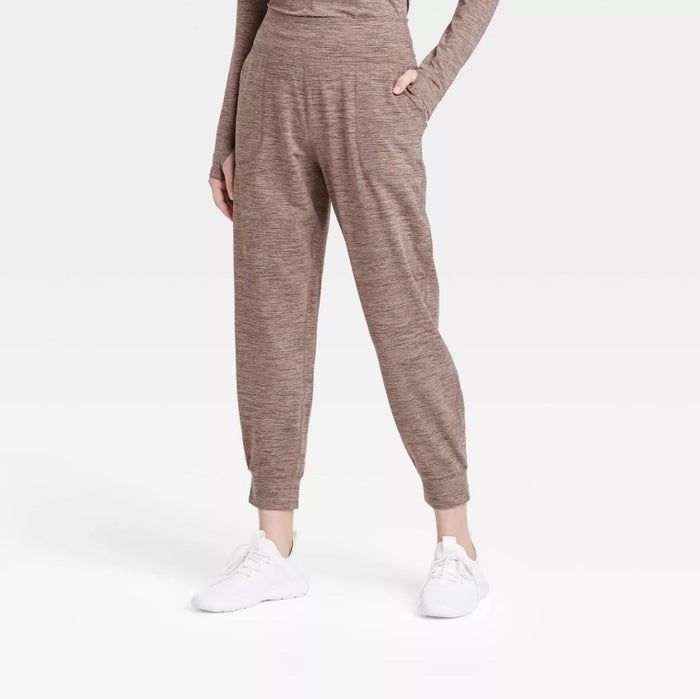 A model styled in light brown joggers paired with a matching long-sleeve top and white shoes, casually posing with one hand in the pocket