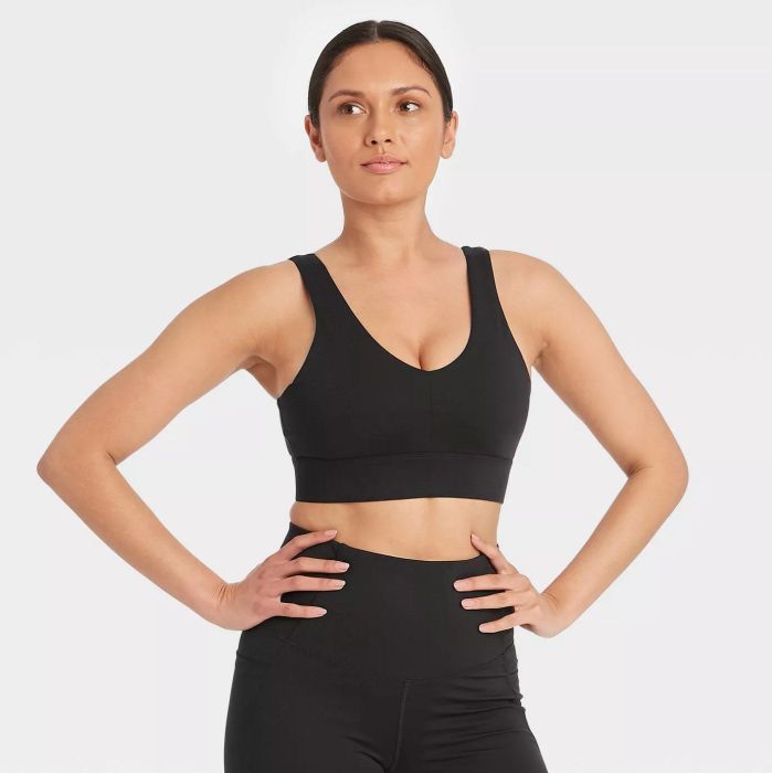 A model posing confidently in the black sports bra paired with black pants, hands resting on their hips