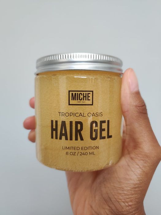 A hand holding a jar of MICHE Tropical Oasis Hair Gel with a light background.