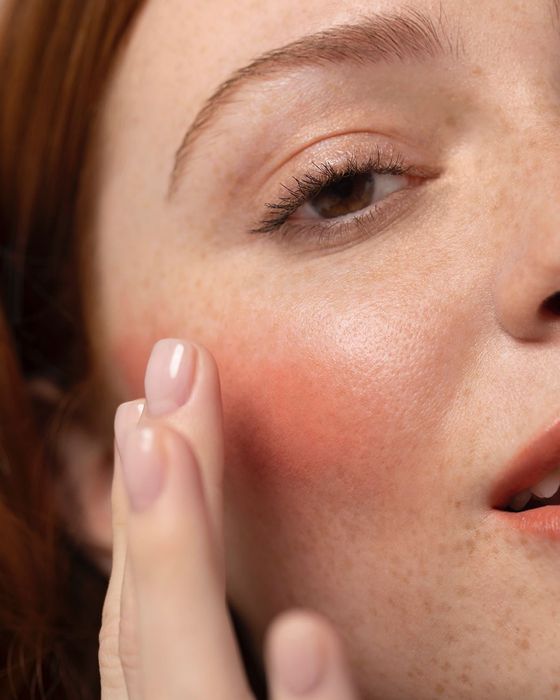 model seamlessly blending the multi-stick formula into their cheek in a soft pink hue