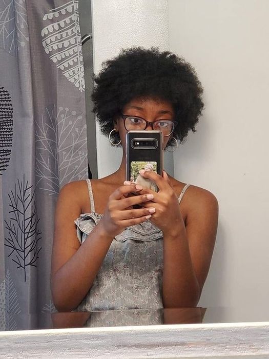 A reviewer with short coily hair showcasing her defined curls after using the product