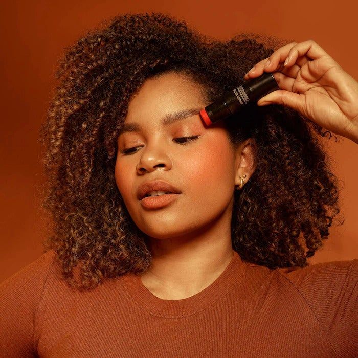 A model holds the Nudestix while it’s applied to their eyelids, cheeks, and lips, giving them a rosy, flushed look.