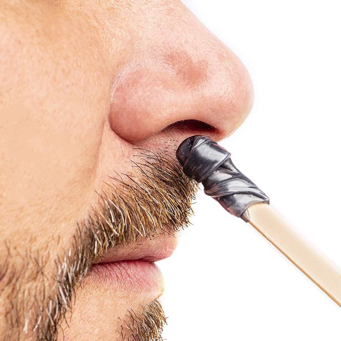 A person uses a popsicle stick to wax their nostril.