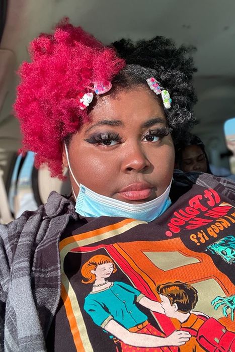 A reviewer with very curly hair shows a striking contrast between half of their hair dyed bright pink and the other half in its natural color.