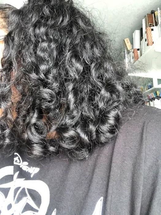 A reviewer showcasing her tight curls after using the scalp massage brush