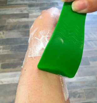 A reviewer using the provided scraper to remove the depilatory cream from their arm