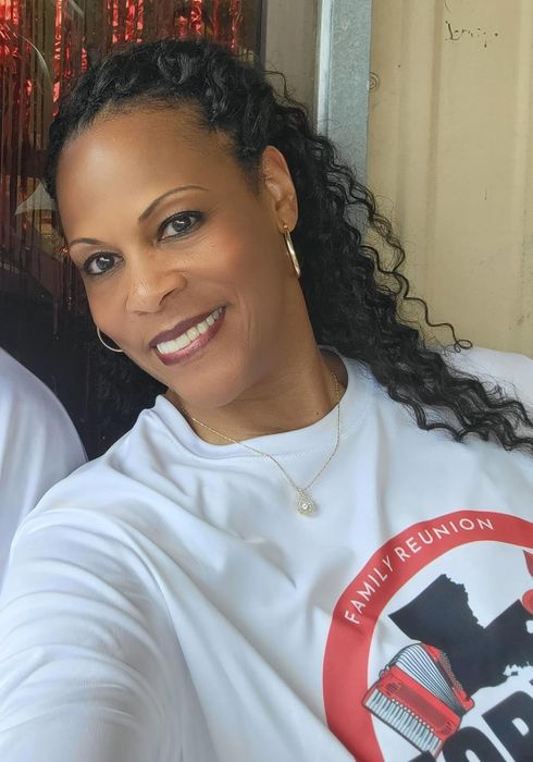 A reviewer wearing a white 'FAMILY REUNION' shirt, smiling for the camera while showcasing their tinted skin serum look.