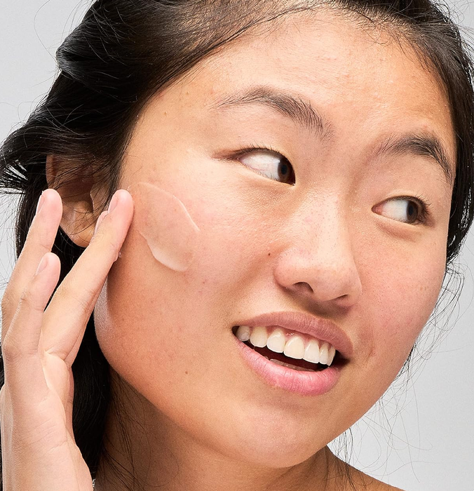 A smiling individual gently applying moisturizer to their cheek