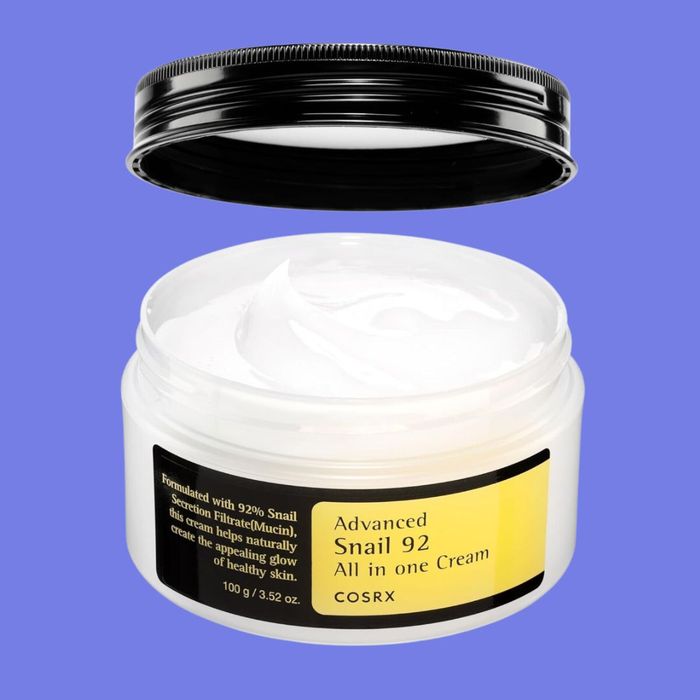 A jar of COSRX Advanced Snail 92 All in One Cream with a black lid removed, showing the white cream inside. The jar features text highlighting 92% Snail Secretion Filtrate.