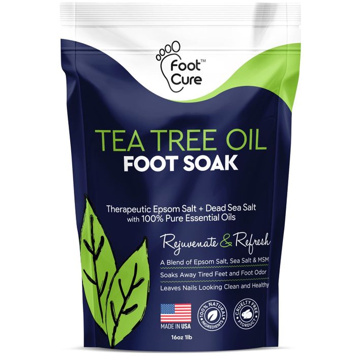 The packaging of Foot Cure Tea Tree Oil Foot Soak is shown, emphasizing its therapeutic blend of epsom salt, dead sea salt, and 100% pure essential oils, designed for foot rejuvenation