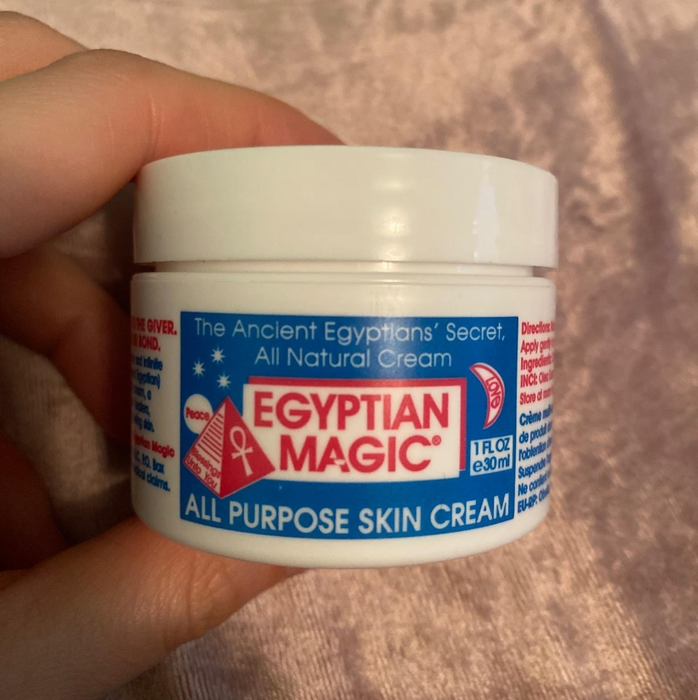 image of a reviewer's hand holding up the small container of cream