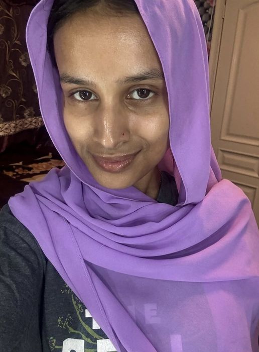 A person in a purple scarf smiles warmly at the camera while indoors.