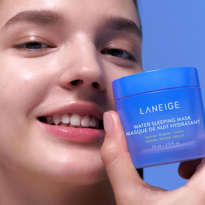 A smiling person holding a Laneige Water Sleeping Mask jar close to their face, showcasing the skincare product
