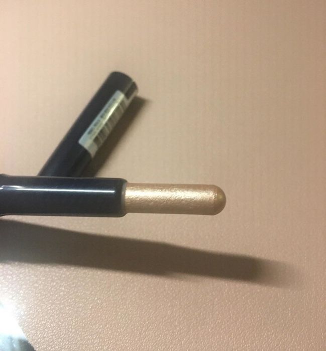 Reviewer displaying the rounded tip, with the full gold stick being lifted from the tube.