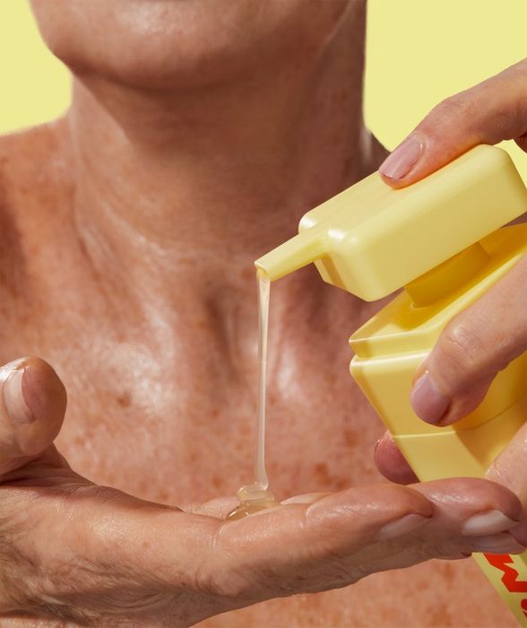A person dispensing a skincare or hygiene product from a yellow bottle into their hand