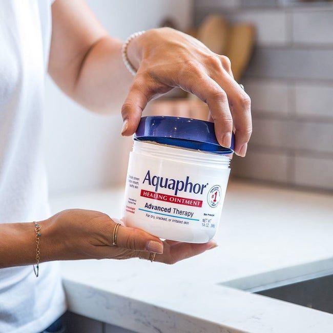 A model holding a jar of Aquaphor ointment.