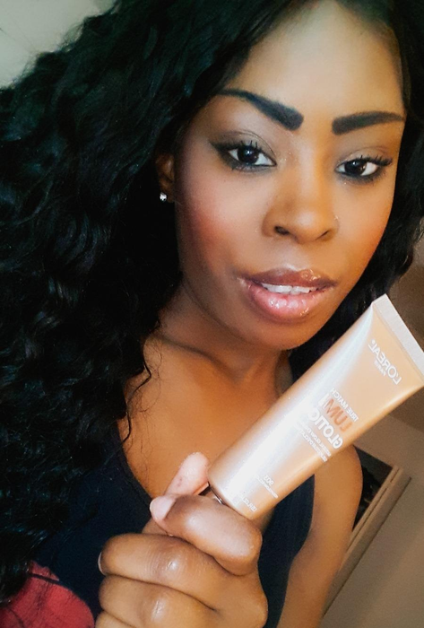 A reviewer with a deeper complexion applying the glowing lotion for a radiant finish