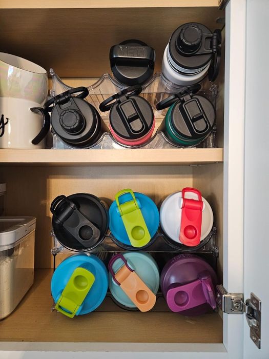 A cabinet neatly arranged with stacks of colorful travel mugs and portable drink containers